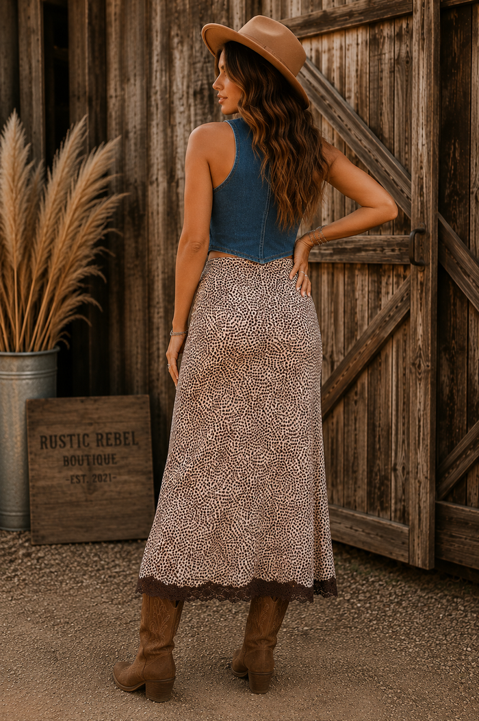 Women's cheetah print maxi skirt featuring ruched detailing, brown lace splicing and a front slit styled with cowboy boots and a denim vest.