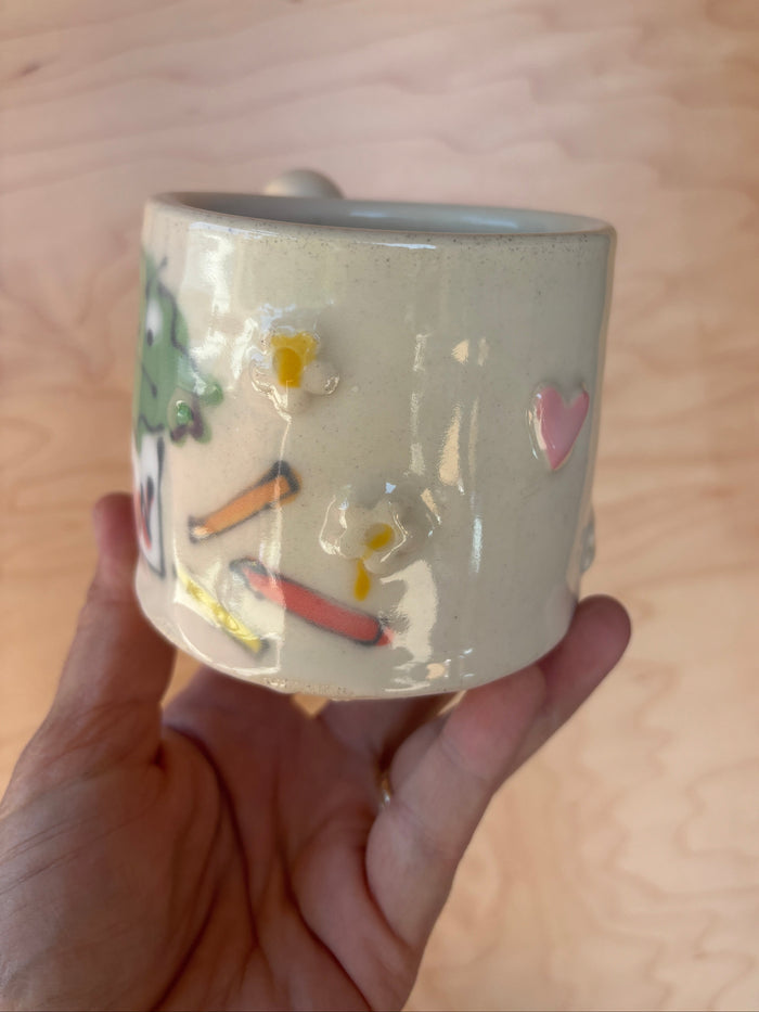 Hand holding a ceramic mug with illustrations on a wooden surface