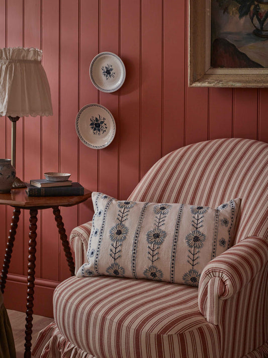 Striped armchair with decorative pillow against a red paneled wall with two hanging plates.