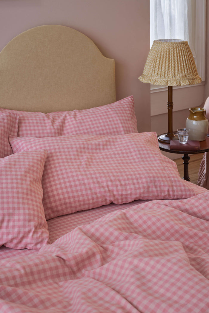 Bed with pink checkered bedding and a lamp on a nightstand.