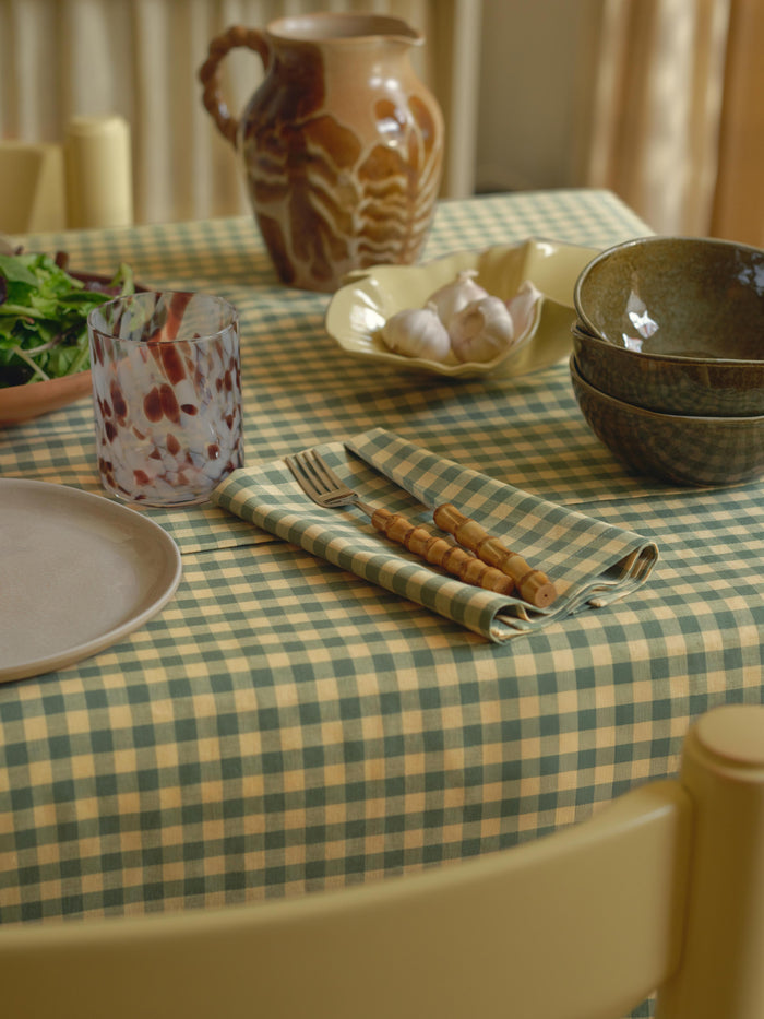 Dining table setting with checkered tablecloth, ceramicware, and cutlery.