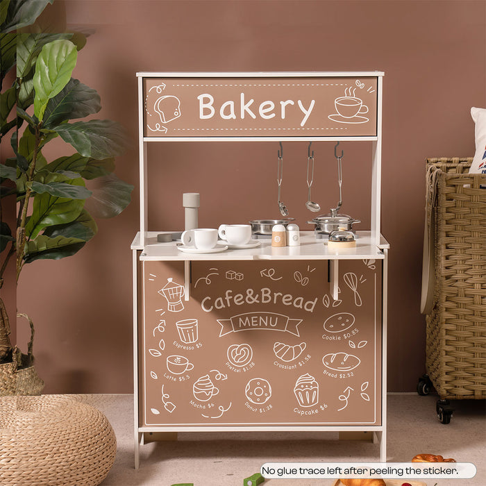 ROBUD cafe bakery play kitchen shown in a living room with rattan accents and chalkboard signage.