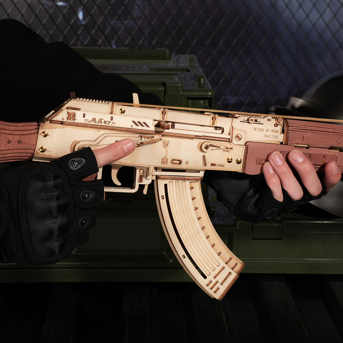 Hands cradling a completed ROKR AK-47 wooden rifle model resting on a green military ammunition crate