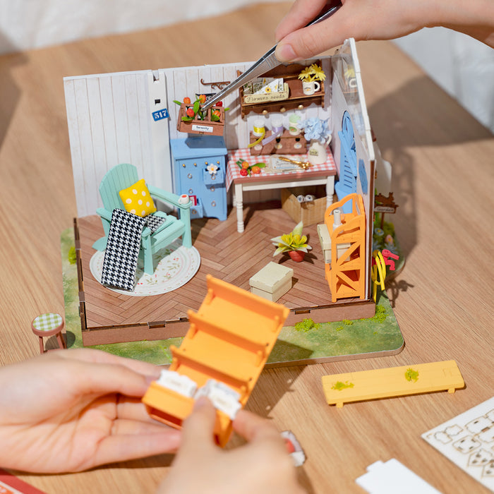 Hands assembling Rolife miniature kitchen scene with blue counter, plants and small wooden details on desk